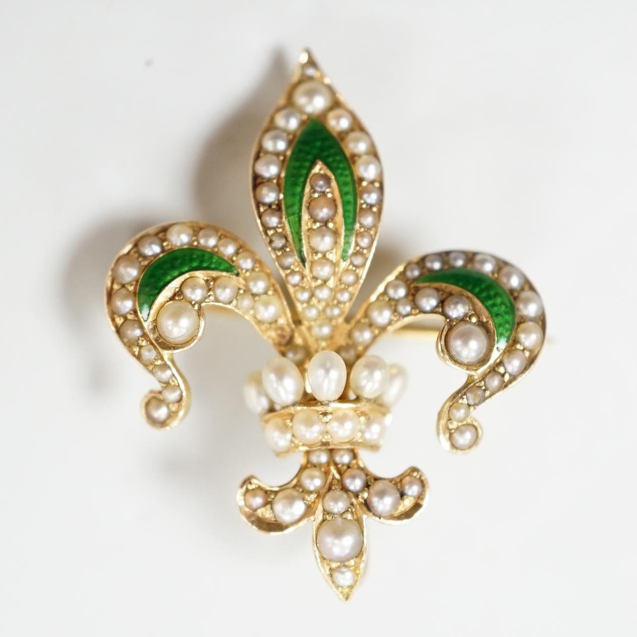 An early 20th century enamelled and pearl set gold fleur de lys brooch, the reverse with pin and suspension loop, 2.75cm., gross 3.7 grams